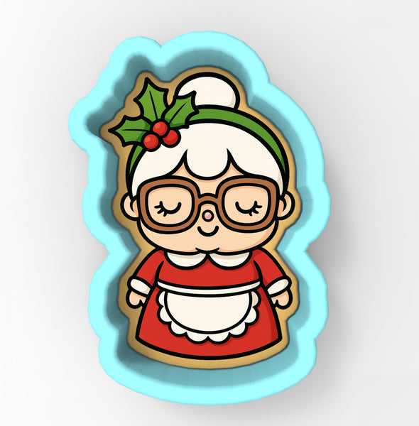 A cookie cutter in the shape of a cartoon character, depicting a smiling woman wearing glasses and a red dress.