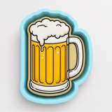 A blue cookie cutter shaped like a mug of beer with a frothy white head.