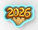 A blue heart-shaped cookie cutter with the number "2026" printed on it, surrounded by gold foil balloons.