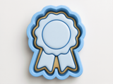 A blue ribbon-shaped cookie cutter with a gold border, designed to cut out cookies shaped like a ribbon.