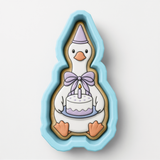 A cookie cutter in the shape of a duck holding a birthday cake.