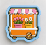 A cookie cutter in the shape of a flower shop window, featuring pink tulips and white daisies in pots.