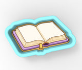 An open book with blank pages, placed on a blue tray or cookie cutter.
