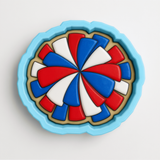 A blue cookie cutter with a colorful design of red, white, and blue shapes on it.