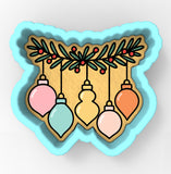 A cookie cutter-shaped design with a festive arrangement of colorful Christmas ornaments hanging from a branch with berries.