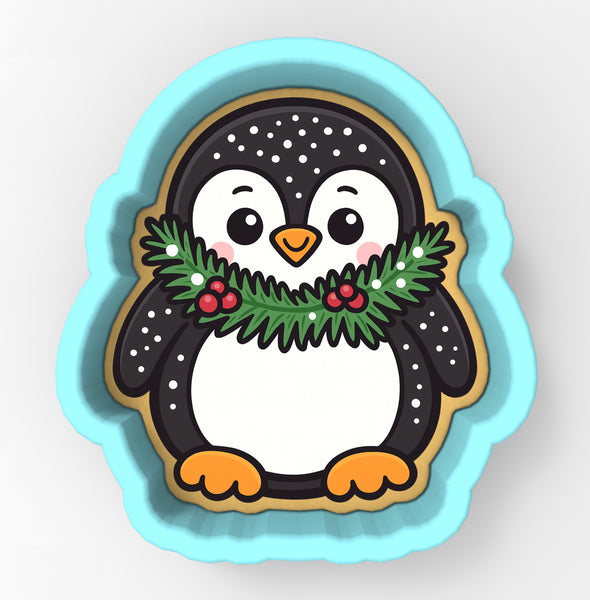 A cute cartoon penguin cookie cutter with a festive wreath around its neck.