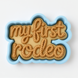 A blue cookie cutter shaped like the word "Rodeo" with the letters arranged in a playful, decorative manner.