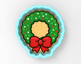 A cookie cutter in the shape of a Christmas wreath, with a red bow on top.