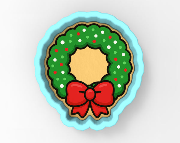 A cookie cutter in the shape of a Christmas wreath, with a red bow on top.