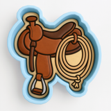 A blue cookie cutter shaped like a brown leather saddle with a rope and a stirrup.