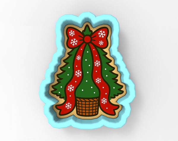 A cookie cutter shaped like a Christmas tree with a red bow and snowflakes, placed in a basket.