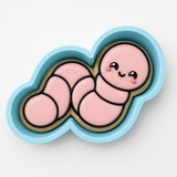 A cookie cutter in the shape of a cute pink caterpillar with a smiling face.