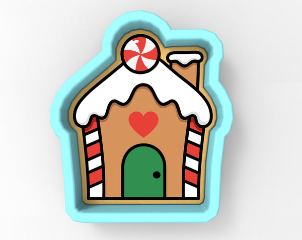 A cookie cutter in the shape of a house with a red heart on the front door and a candy cane on top.