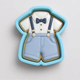 A cookie cutter in the shape of a baby's outfit, including a white shirt, blue pants, and a blue bow tie.