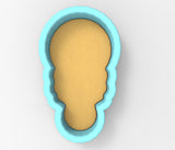 A blue-colored cookie cutter in the shape of a face, with a yellow dough-like substance inside.