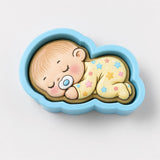 A baby cookie in a blue cloud-shaped container is depicted, with a pacifier in its mouth and a sleeping expression.