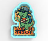 A cartoon dinosaur wearing sunglasses and a baseball cap, holding a pencil and a stack of books, with the text "BACK TO SCHOOL" below.