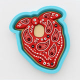 A red paisley-patterned cookie cutter in a blue mold.