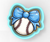 A cookie cutter shaped like a baseball with a blue bow on top.