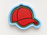 A red baseball cap is depicted in a blue and gold cookie cutter shape against a white background.