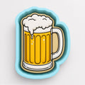 A blue cookie cutter shaped like a mug of beer with a frothy white head.