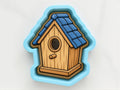 A birdhouse cookie cutter in the shape of a house with a blue roof and wooden exterior.