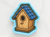 A birdhouse cookie cutter in the shape of a house with a blue roof and wooden exterior.
