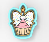 A cookie cutter in the shape of a cupcake with a candle and sprinkles on top.