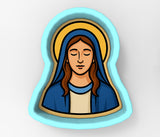 A blue oval-shaped cookie cutter depicting a woman with long brown hair wearing a blue robe and a halo.