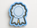 A blue ribbon-shaped cookie cutter with a gold border, designed to cut out cookies shaped like a ribbon.