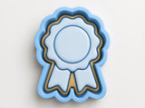 A blue ribbon-shaped cookie cutter with a gold border, designed to cut out cookies shaped like a ribbon.
