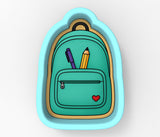 A cookie cutter in the shape of a backpack, with a pencil and a heart symbol inside the pocket.