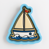 A cookie cutter shaped like a sailboat with a red flag on top, set against a blue background.