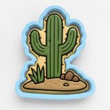 A cookie cutter in the shape of a cactus, with a sandy ground and some small rocks around it.
