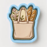 A cookie cutter in the shape of a bag, with a handle and two breadsticks inside.