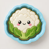 A cheerful cartoon cauliflower with a smiling face, surrounded by green leaves, is depicted in a blue bowl.