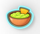 A bowl of guacamole with a tortilla chip on top, depicted in a cookie cutter shape.