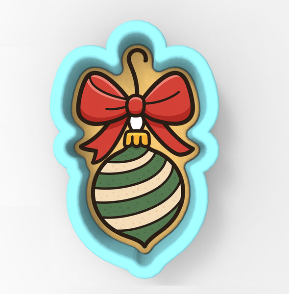 A cookie cutter shaped like a Christmas ornament with a red bow and green and white striped pattern.