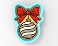 A cookie cutter in the shape of a cat's head with a red bow and a striped ornament.