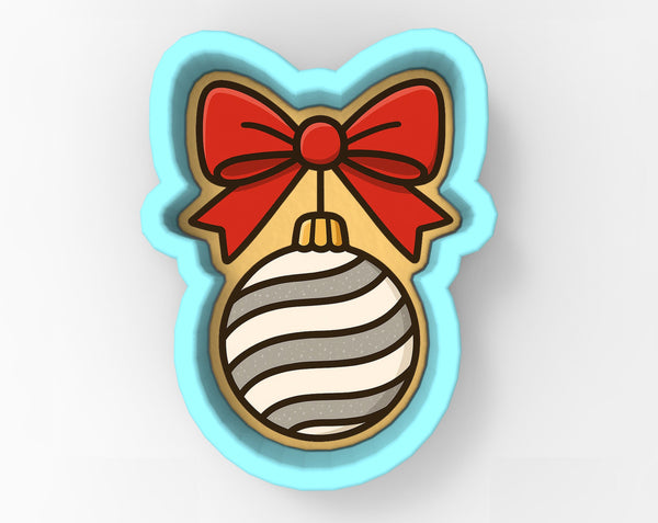 A cookie cutter in the shape of a cat's head with a red bow and a striped ornament.