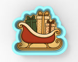 A cookie cutter-shaped illustration depicting a red sled carrying three gift boxes in various colors and patterns.