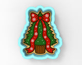 A cookie cutter shaped like a Christmas tree with a red bow and snowflakes, placed in a basket.