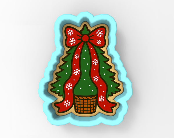 A cookie cutter shaped like a Christmas tree with a red bow and snowflakes, placed in a basket.