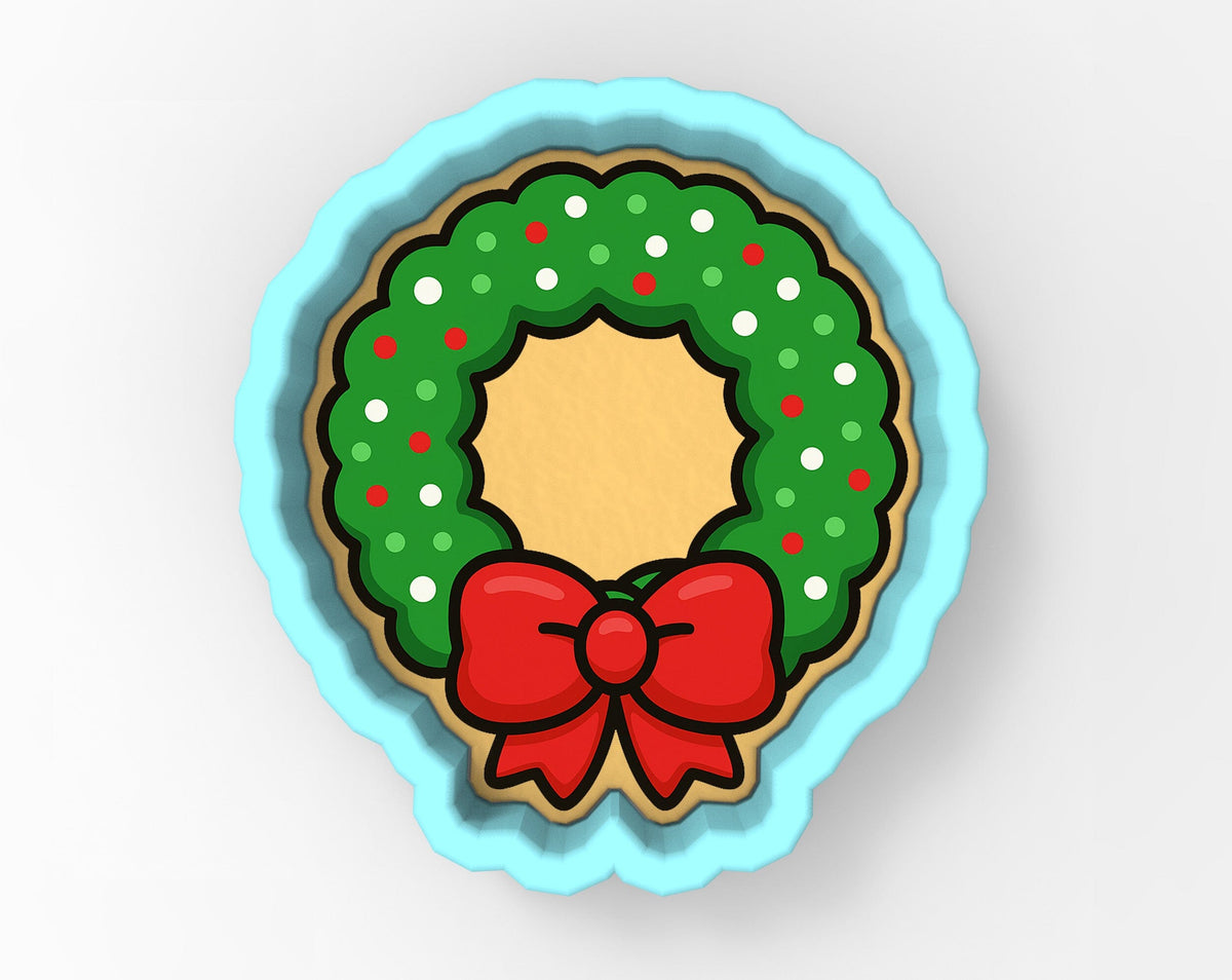 A cookie cutter in the shape of a Christmas wreath, with a red bow on top.