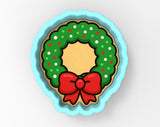 A cookie cutter in the shape of a Christmas wreath, with a red bow on top.