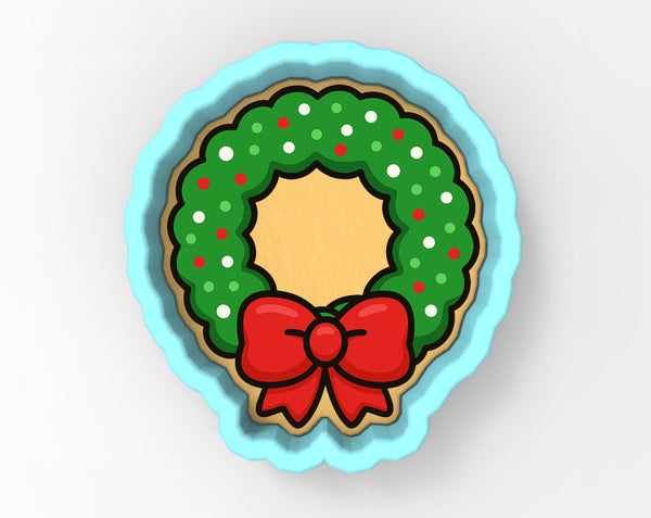 A cookie cutter in the shape of a Christmas wreath, with a red bow on top.