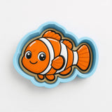 A toy shaped like a clownfish, with a bright orange body and white stripes, is depicted in a blue and white cookie cutter.