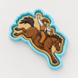 A cowboy riding a bucking horse in a cookie cutter-shaped design.