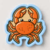A cookie cutter in the shape of a crab with orange claws and a beige body.