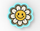 A blue flower-shaped cookie cutter with a smiling yellow flower on it.